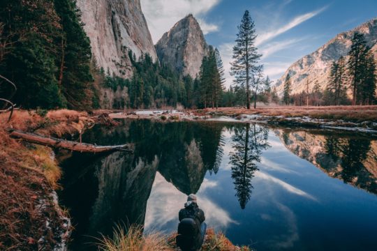 person sitting on rock looking at body of water near forest during daytime