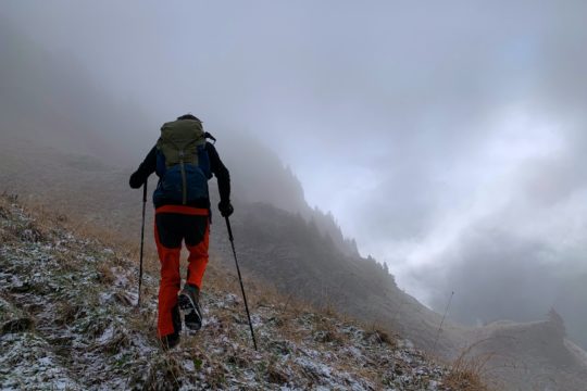 man in green jacket and red backpack walking on rocky road