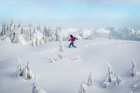 person in red jacket and black pants walking on snow covered ground during daytime
