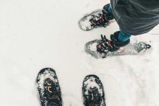person in black pants and black and white snow ski shoes standing on snow covered ground
